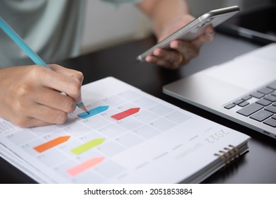 Event planner timetable agenda plan on year 2022 schedule event. Business woman checking planner on mobile phone, taking note on calendar desk on office table. Calendar event plan, work planning - Shutterstock ID 2051853884