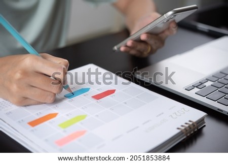 Event planner timetable agenda plan on year 2024 schedule event. Business woman checking planner on mobile phone, taking note on calendar desk on office table. Calendar event plan, work planning