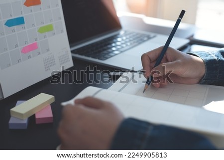 Event planner timetable agenda plan on year 2023 schedule event. Business woman checking timetable, taking note on calendar planner notebook on office table. Calendar event plan, work planning