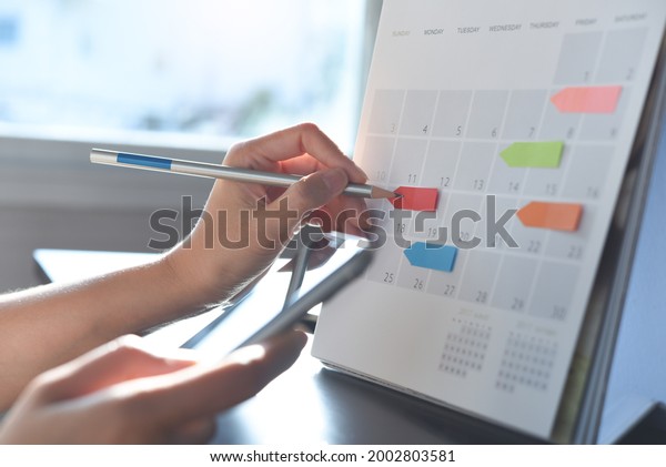 Event\
planner timetable agenda plan on schedule event. Business woman\
checking planner on mobile phone, taking note on calendar desk on\
office table. Calendar event plan, work\
planning