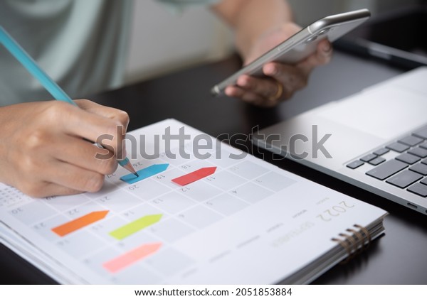 Event planner timetable agenda plan on year 2022
schedule event. Business woman checking planner on mobile phone,
taking note on calendar desk on office table. Calendar event plan,
work planning