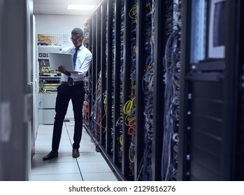 Every Calculation Counts. Cropped Shot Of A IT Technician Working On His Laptop While Standing Inside Of A Server Room.