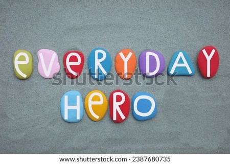 Everyday hero, creative slogan, logo and motivational message composed with hand painted multi colored stone letters over green sand for a unique slogan