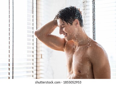 Everyday Hygiene Routine Concept. Side View Portrait Of Smiling Young Guy Taking A Shower Standing Under Falling Water Drops Washing Naked Body And Head In Bathroom At Home. Male Bodycare