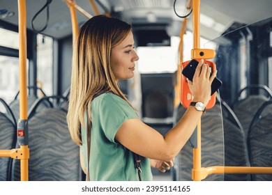 Everyday life and commuting to work by bus. Young Caucasian businesswoman is paying transport ticket with mobile phone.