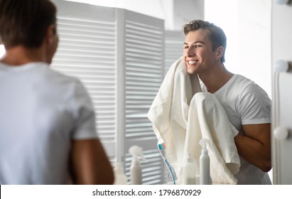Everyday Routine Concept. Good-looking man wiping his face with towel while standing in modern bathroom