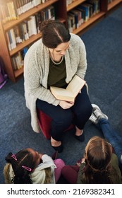 Everyone Loves A Good Story. High Angle Shot Of A Teacher Reading To A Group Of Elementary School Kids In The Library.