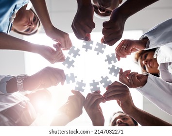Everyone plays their part here. Low angle shot of a group of doctors forming a huddle while each holds a puzzle piece inside of a hospital.