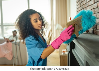 Everything Is Clean. Careful Young Nurse Cleaning The Apartment From Dust While Helping Her Patient