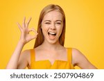 Everything is Great. Beautiful Young Girl Winking And Showing Ok Sign, Standing Over Yellow Background With Copy Space