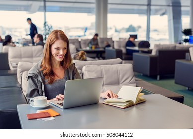 Everything looks great. Beautiful young woman using laptop and notebook while sitting in waiting hall at airport