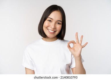 Everything Okay. Smiling Young Asian Woman Assuring, Showing Ok Sign With Satisfied Face, Standing Over White Background