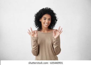 Everything is perfect. Happy positive dark-skinned student girl showing OK gesture with both hands, having good mood after passing all exams at college successfully. Human emotions and body language