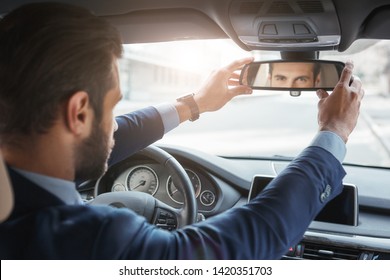 Everything should be perfect. Back view of young and handsome bearded businessman in formal wear adjusting the rearview mirror while driving his car. - Powered by Shutterstock