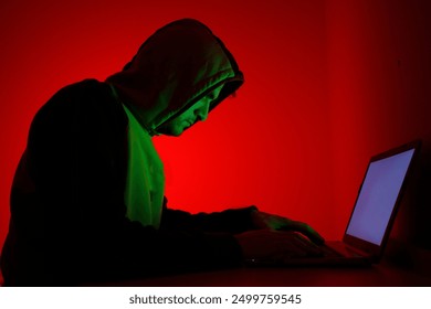 The evil hacker is working in front of his laptop.
A person sits focused in a dimly lit space, illuminated by a striking red background and green lighting.  - Powered by Shutterstock