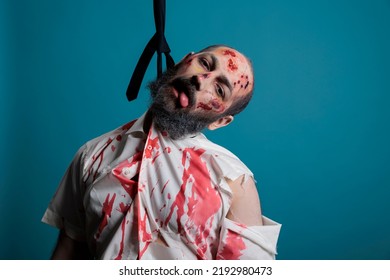 Evil Halloween Monster Hanged At Gallows With Hanging Rope, Suicidal Creepy Zombie At Execution In Front Of Studio Camera. Frightening Dangerous Corpse Hangs From Knot Thinking About Suicide.