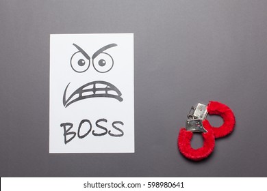  Evil painted boss face with red handcuffs on a white paper  isolated gray background.Sexual harassment concept.