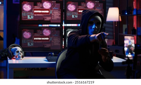Evil programmer concealing identity using mobile phone to film ransom video in secret base. Scammer with anonymous mask using cellphone to record blackmail footage, threatening victims, camera A