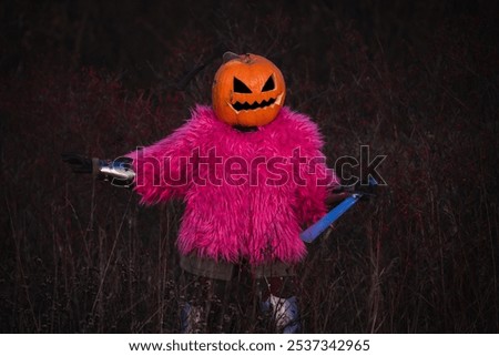 An evil scarecrow in a jack o lantern on his head poses in a night field with an axe stuck in a pumpkin. The Halloween concept.