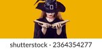 Evil witch reading book of spells. Beautiful young woman dressed as witch with bloody cut on her neck hiding her face under hat and looking through her witchcraft manual. Halloween and magic concept