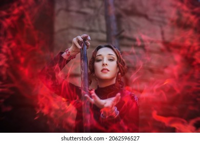 Evil witch with a staff in the forest. Slavic witch creates red magic. A young woman in a black dress and a crown embroidered with beads. Halloween costume fantasy