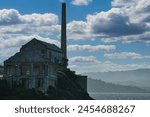 Evocative sunset behind the haunting silhouette of an old industrial building, on Alcatraz Island, casting a glow over its decaying facade