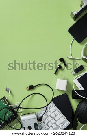 E-waste flat lay: keyboard, phone, headphones, accessories framing bottom right corner of green background. Ample copy space provided.