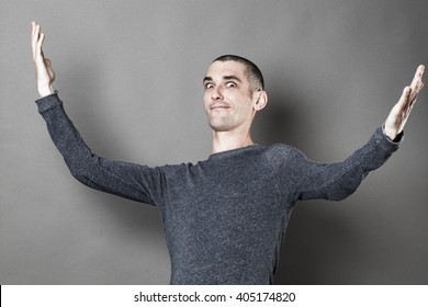 exaggeration concept -  expressive young man with eyes wide open opening his arms wide for theater play or lyric show off, grey background studio
