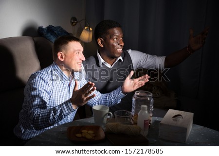 Exalted male friends watching matchup on tv together at home at evening 