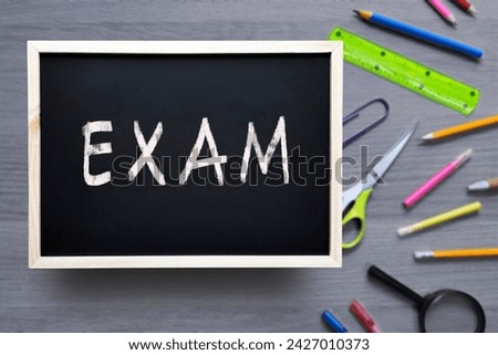 Exam word written with white chalk on school blackboard. Concept of study, knowledge, test, preparation for exams.