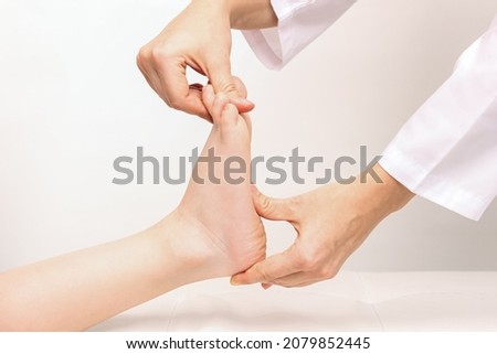 Examination of a child by an orthopedist. Cropped shot of female doctor holding a kid's foot in her hands.Pathology of bone structures, flat feet, injury. Foot treatment. Pain from uncomfortable shoes