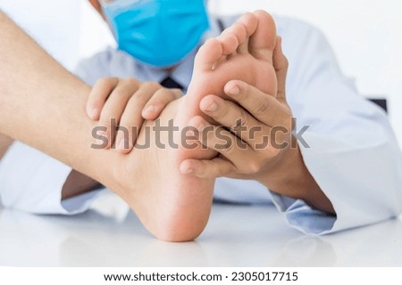 Examination of a young woman by an orthopedist.White uniform male doctor holding a girl's foot in his hands. Flat feet, injury. Foot treatment. Pain from uncomfortable shoes.Medical orthopedic unit.