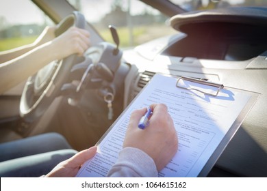 Prüfprüfer füllt das Formular für den Führerscheintest aus und sitzt mit ihrem Schüler in einem Auto