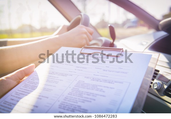 Examiner filling in driver\'s license road\
test form sitting with her student inside a\
car