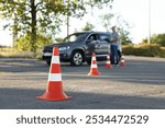 Examiner instructing student before exam at driving school test track, focus on traffic cone