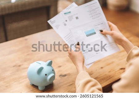 Examining financial documents while planning savings with a piggy bank on a wooden table in a cozy indoor setting