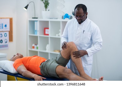 Examining knee. Physical therapist examining knee of sportsman lying near him after getting injury
