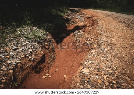 an example of erosion, gully or rill erosion, caused by the movement of water across the land surface on a hillside road.