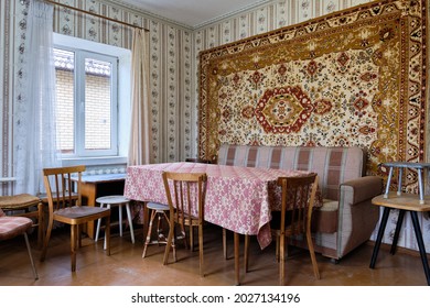 Example of Old Soviet Russian poor interior in Khruschev House. Aged table, chairs, sofa. Shabby floor. Tattered wallpaper and carpet as decor on the wall. Apartment of pensioners.