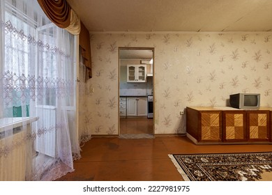 Example of Old Soviet Russian poor interior in Khruschev House. Aged sideboard, tv set, curtains, kitchen furniture. Shabby floor. Tattered wallpaper on wall. Carpet as decor. Apartment of pensioners. - Shutterstock ID 2227981975
