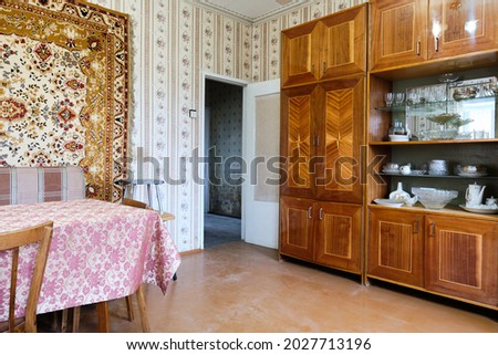 Example of Old Soviet Russian poor interior in Khruschev House. Aged  sideboard, table, chairs, sofa. Shabby floor. Tattered wallpaper on the wall. Apartment of pensioners. Selective focus.