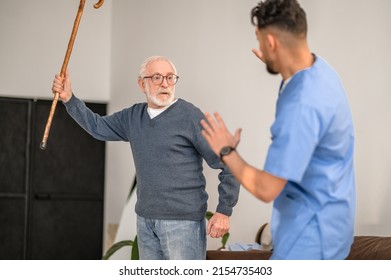 Exasperated pensioner threatening his caretaker with his cane - Shutterstock ID 2154735403