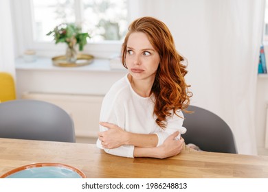 Exasperated woman blowing out her lips as she glances aside with wide eyes while sitting relaxing at a table in a high key room with copyspace