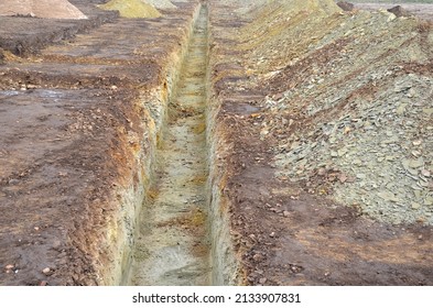 Excavation For Laying Utility Networks, Sewer Pipes, Electric Cables Or Gas Connections To New Buildings. Digging Heavily Scattered Rocky Soil. Trench War Effort To Protect Infantry