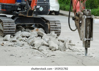 Excavator breaking concrete road surface with hydrohammer drill at repairing roadwork