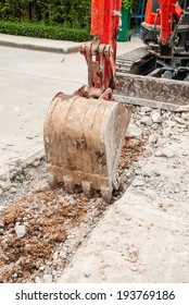 Excavator breaking concrete road surface. Shows part of the excavator bucket.