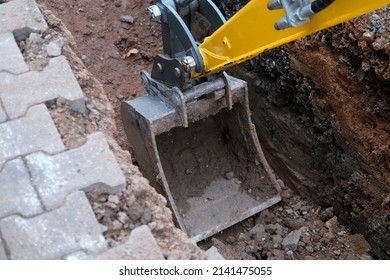 excavator bucket digs earth in trench on street, concept of repairing urban communications, conducting electrical networks to buildings, underground laying optical fiber for communication