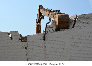 An excavator bucket dismantles an old brick wall