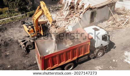 Excavator bucket loads industrial debris into truck. Process of demolishing and destruction old house. Release of quarters for new development