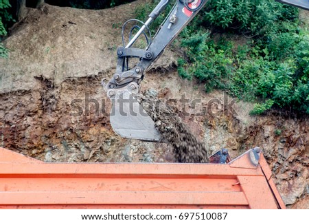 Excavator bucket loads stones and dirt into the truck body